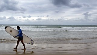 a surfer walks along the beach after surfing in Coffs Harbour, Australia