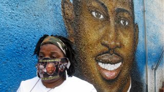 Thea Brooks stands in front of a mural of Ahmaud Arbery, her slain nephew