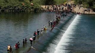 FILE - In this Sept. 18, 2021, file photo Haitian migrants use a dam to cross into the United States from Mexico in Del Rio, Texas. President Joe Biden embraced major progressive policy goals on immigration after he won the Democratic nomination, and he has begun enacting some. But his administration has been forced to confront unusually high numbers of migrants trying to enter the country along the U.S.-Mexico border and the federal response has inflamed both critics and allies.