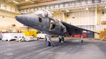 A fighter jet with no engines sits in the hangar bay of a ship