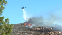 A helicopter drops water onto a brush fire in Santee on Nov. 25, 2021.