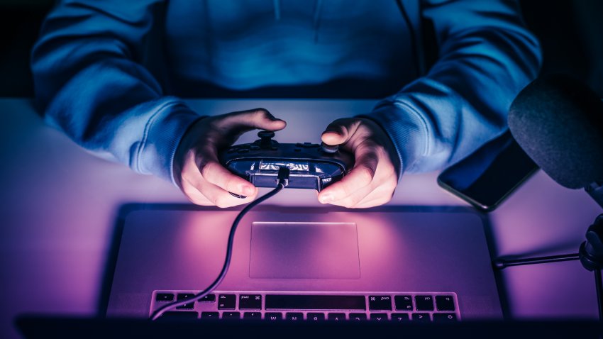 Close up view of young hands using a game pad with laptop to play games online.