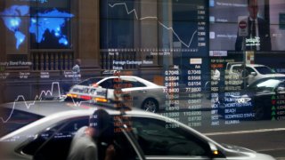 Vehicles are reflected in a window as electronic boards display stock information at the Australian Securities Exchange, operated by ASX.