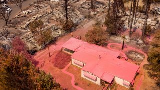 An aerial view shows a home covered in fire retardant near dozens of properties destroyed at the Creekside Mobile Home Park after the Cache fire ripped through the area in Clearlake, California on August 19, 2021 as Wildfire continue to burn across the state.