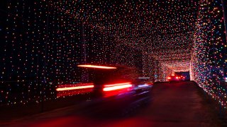Passenger vehicles move through a tunnel of holiday lights