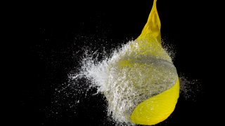 Yellow waterballoon bursting against black background, close up