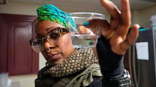 Angela Stamps holds a sampling of tap water, Jan. 6, 2022, in Flint, Michigan.