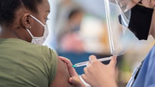 School nurse administering a vaccine to a masked student.