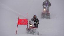 Course workers blow snow from the men's giant slalom course as the snow comes down at the alpine ski venue at the 2022 Winter Olympics, Sunday, Feb. 13, 2022, in the Yanqing district of Beijing.