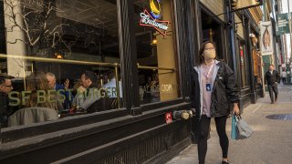 A pedestrian wearing a protective mask walks past a restaurant on Sacramento Street in San Francisco, California, on Feb. 16, 2022.