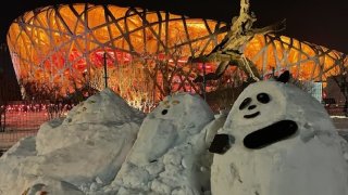 A snow panda (right) sits in front of the "Bird's Nest" at the Winter Olympics in Beijing, Feb. 16, 2022.