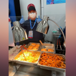 A man gives a thumbs up behind a food counter serving fried food like onion rings and fries at a dining hall in Beijing, Feb. 8, 2022.