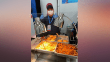 A man gives a thumbs up behind a food counter serving fried food like onion rings and fries at a dining hall in Beijing, Feb. 8, 2022.