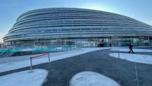 A person (right) walks by the National Speed Skating Oval, also called the "Ice Ribbon," at the Winter Olympics on a cold day in Beijing, Feb. 15, 2022.