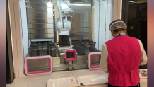 A dining hall employee lines up trays in front of an automated food system in Beijing, Feb. 8, 2022.