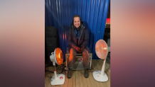 NBC 7 Anchor Steven Luke sits in between heaters to warm up before going on air during the Winter Olympics in Beijing, Feb. 16, 2022.