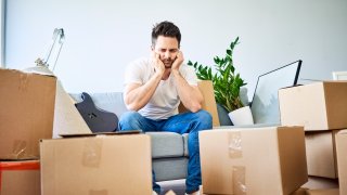 Frustrated man sitting on couch surrounded by cardboard boxes