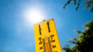 A close up of a yellow thermometer against a bright sunlit sky.