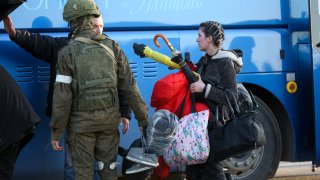 A woman who left a shelter in the Metallurgical Combine Azovstal walks to a bus escorted by a serviceman of Donetsk People's Republic militia in Mariupol, in territory under the government of the Donetsk People's Republic, eastern Ukraine, Friday, May 6, 2022.