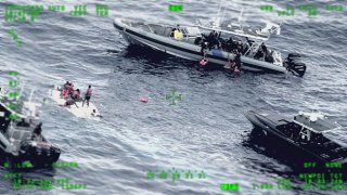 This photo released by the Seventh U.S. Coast Guard District shows people standing on a capsized boat, left, as some of its passengers are pulled up on to a rescue boat, top, in the open waters northwest of Puerto Rico, May 12, 2022.