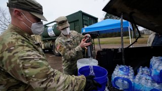 Mississippi Army National Guard Sgt. Chase Toussaint, right, and Staff Sgt. Matthew Riley, both with the Maneuver Area Training Equipment Site of Camp Shelby, fill 5-gallon water drums