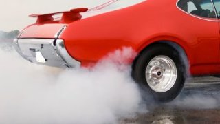 Stock photo of a classic red car spinning out its tires, causing smoke.
