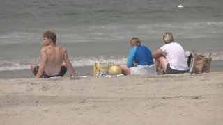 Three people sitting on the beach facing the water