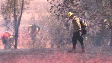 Fire crews walk through pink-retardant-covered ground at the scene of a brush fire near the Ramona Airport on July 19, 2022.