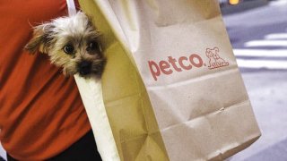 A customer carries a dog near a Petco Animal Supplies shopping bag outside a store in New York.