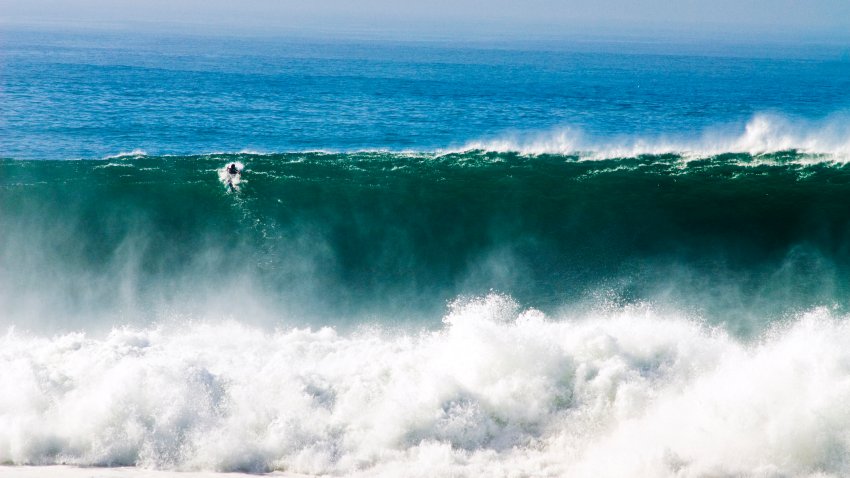 A surfer paddles over a giant wave at Blacks Beach in San Diego, California