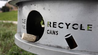 A wine bottle is left in a recycle and trash can.