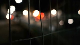 A file photo of a dark street with car lights blury but visible in the background.