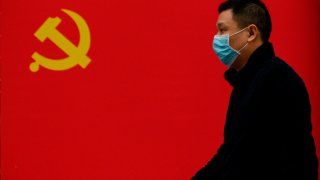 A man wearing a face mask as a preventive measure against Covid-19 walks past a Communist Party flag in Wuhan, China, on March 31, 2020.
