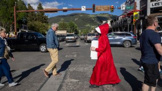 Abortion rights protester Caitlin Devore, dressed as a “handmaiden” crosses a street to join a a gathering to protest the Supreme Court’s decision in the Dobbs v Jackson Women’s Health case on June 24, 2022 in Jackson Hole, Wyoming.