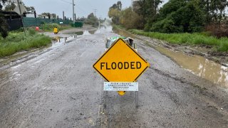 A sign that reads "flooded" is placed in the center of a road in San Ysidro on a rainy day, as seen on Wednesday, March 15, 2023.