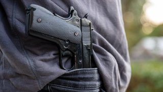 Gloved hand carrying a pistol in his pants, blur nature background,