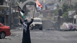 A Palestinian man waves Palestinian and Syrian flags in front of an Israeli army vehicle during a military raid in the Jenin refugee camp, a militant stronghold, in the occupied West Bank, Tuesday, July 4, 2023. Palestinian health officials said at least 10 Palestinians were killed in the operation, which began Monday.