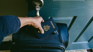 Close-up of unrecognizable black woman at front door preparing to leave house with packed suitcase and passport