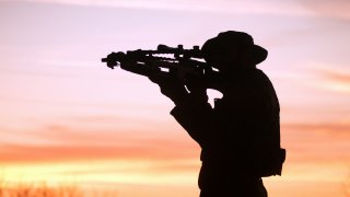 A person aiming with a crossbow at sunset.