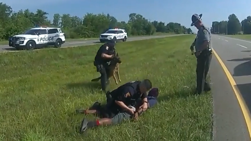 Body cam image of police officer pulling German shepherd away from man on ground.