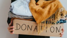 Woman holding cardboard donation box full with clothes. Concept of volunteering work, donation and clothes recycling. Helping poor people
