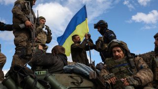 Ukrainian soldiers adjust their national flag atop a personnel armored carrier on a road near Lyman, in the Donetsk region, on Oct. 4, 2022.