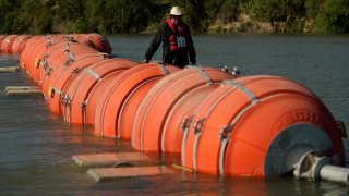 FILE – A kayaker walks past large buoys being used as a floating border barrier on the Rio Grande, Aug. 1, 2023, in Eagle Pass, Texas. A federal judge on Wednesday, Sept. 6, ordered Texas to move a large floating barrier to the riverbank of the Rio Grande after protests from the the U.S. and Mexican governments over Republican Gov. Greg Abbott’s latest tactic to stop migrants from crossing America’s southern border. (AP Photo/Eric Gay, File)