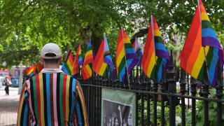 File. A person wearing a sweater with ‘Progress Pride Flag’ colors, including rainbow and black and brown stripes for communities of color, walks past rainbow flags at the Stonewall National Monument, the first US national monument dedicated to LGBTQ history and rights, marking the birthplace of the modern lesbian, gay, bisexual, transgender, and queer civil rights movement, on June 1, 2020 in New York City.