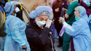 A medical worker reacts as police officers and pedestrians cheer medical workers outside NYU Medical Center in New York, April 16, 2020. Some states that stockpiled millions of masks and other personal protective equipment during the coronavirus pandemic are now throwing the items away.