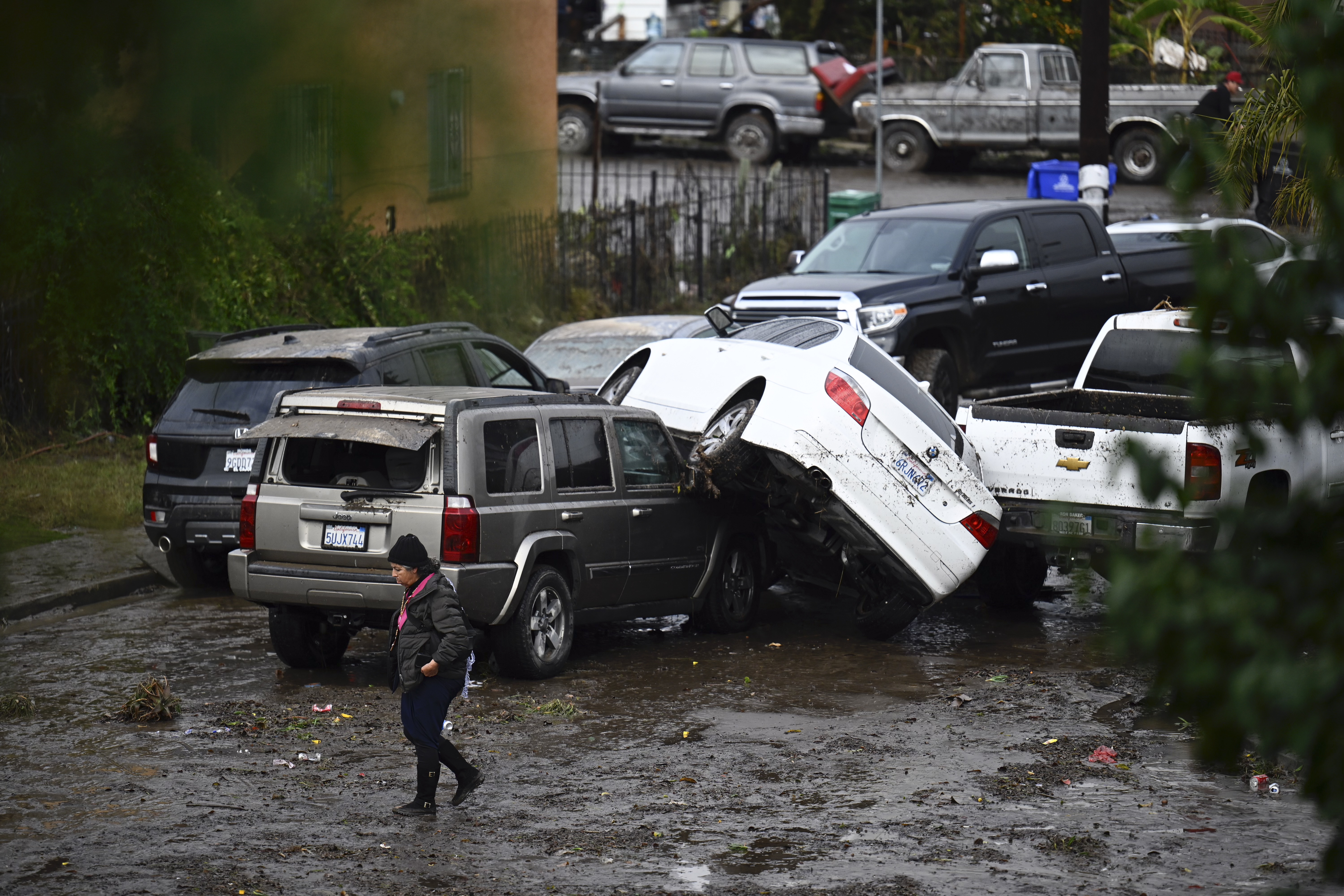 A woman walks by cars damaged by floods during a rainstorm in San Diego on Monday, Jan. 22, 2024.