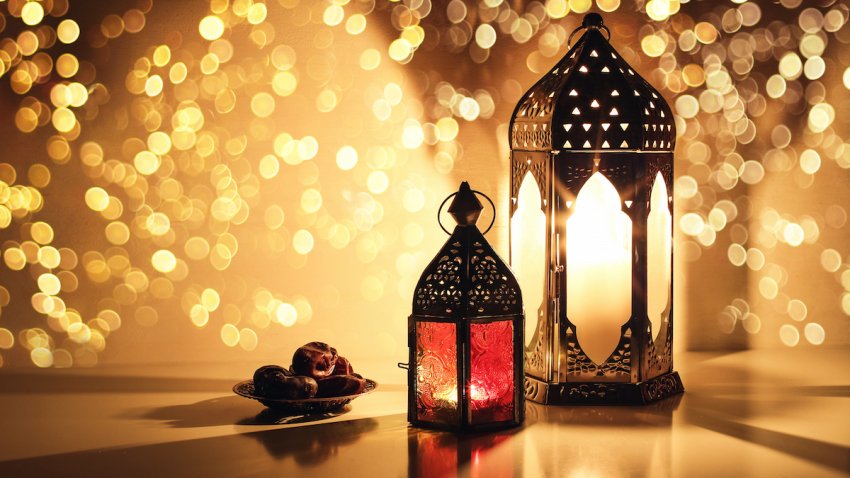 Ornamental Arabic lanterns with burning candles. Glittering golden bokeh lights. Plate with date fruit on the table. Greeting card for Muslim holiday Ramadan Kareem, iftar dinner background.