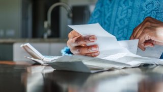 Close-up of Black woman reviewing receipts at kitchen table with sunlight illuminating hands