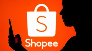 BRAZIL – 2022/03/22: In this photo illustration, a woman’s silhouette holds a smartphone with a Shopee logo in the background. (Photo Illustration by Rafael Henrique/SOPA Images/LightRocket via Getty Images)