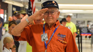 A man in an orange shirt salutes the camera.